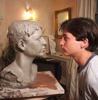 A young boy face to face with his completed bust in clay